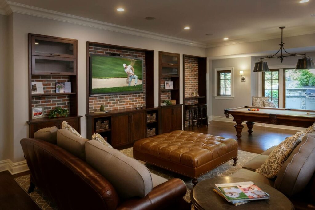 Warm and inviting living room with custom-built cabinet storage flanking a flat-screen TV, set against a backdrop of exposed brick.
