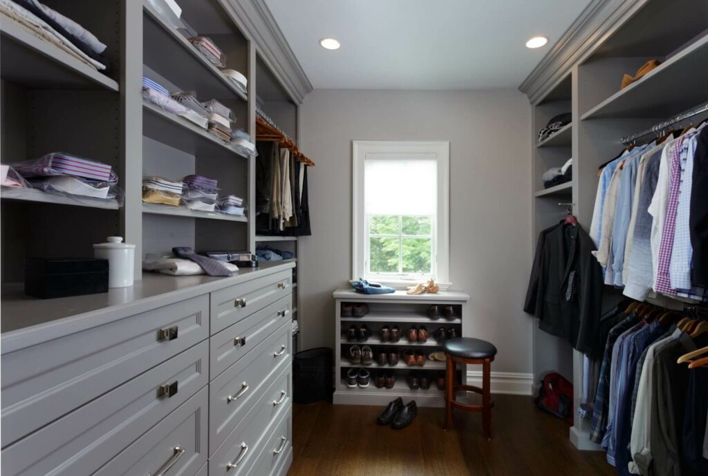 Elegant walk-in closet featuring expansive cabinet storage with drawers and shelves, alongside a window-seat shoe display.
