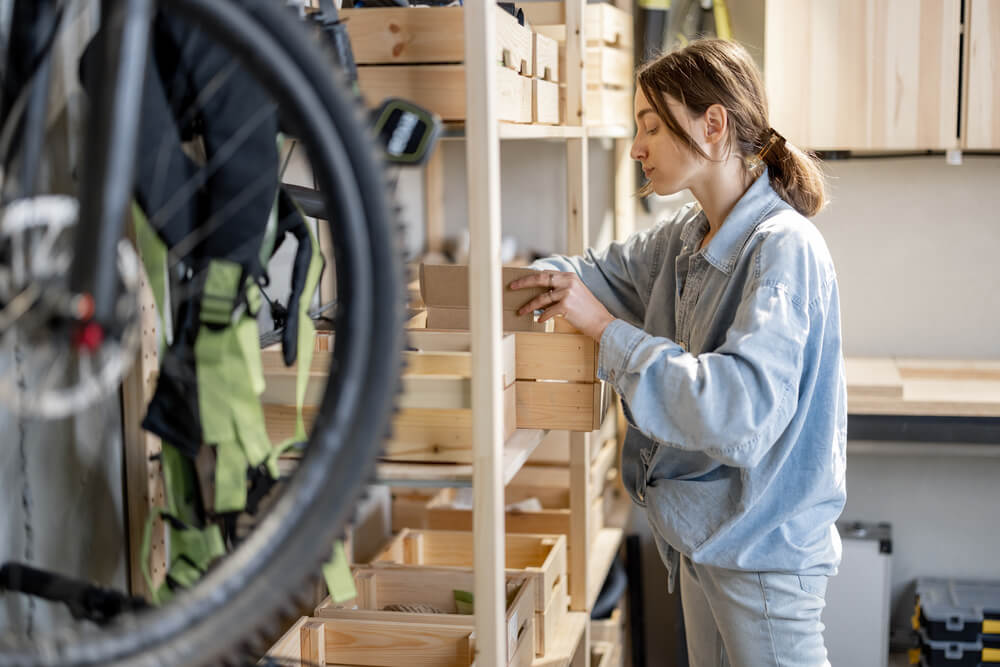 Woman arranging tools in wooden cabinet storage drawers in a well-organized workshop space.