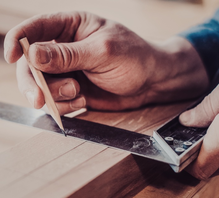 Close-up of a craftsman's hands marking a wooden board with a pencil, precision in bespoke cabinetry making.