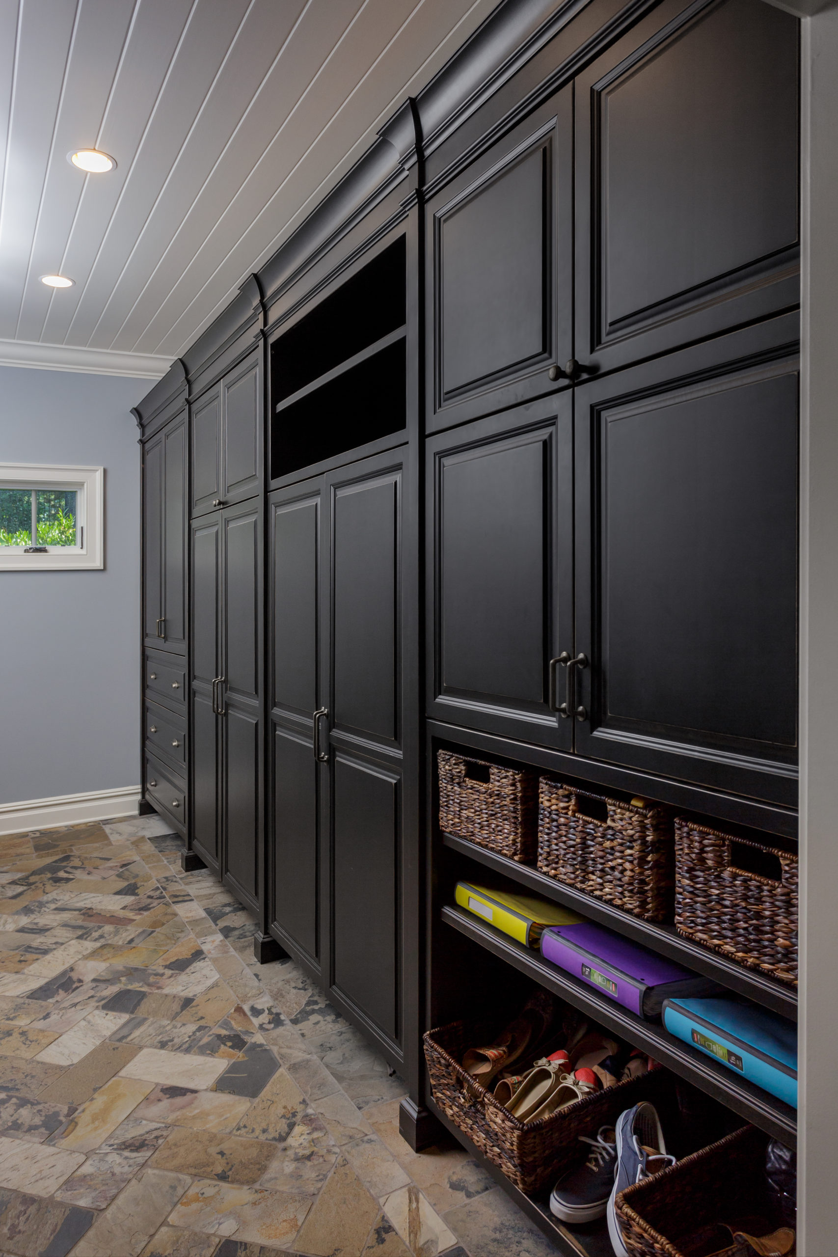 A stylish mudroom featuring black custom cabinetry with a bench, shoe storage shelves, and sleek hardware, set against a black and white checkered floor.