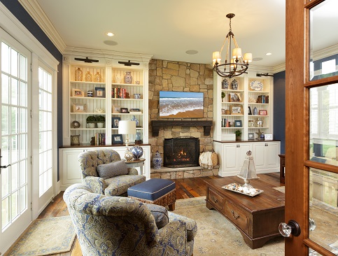 A welcoming living room with custom white bookcases surrounding a stone fireplace, showcasing hardwood floors and French doors that flood the space with natural light.