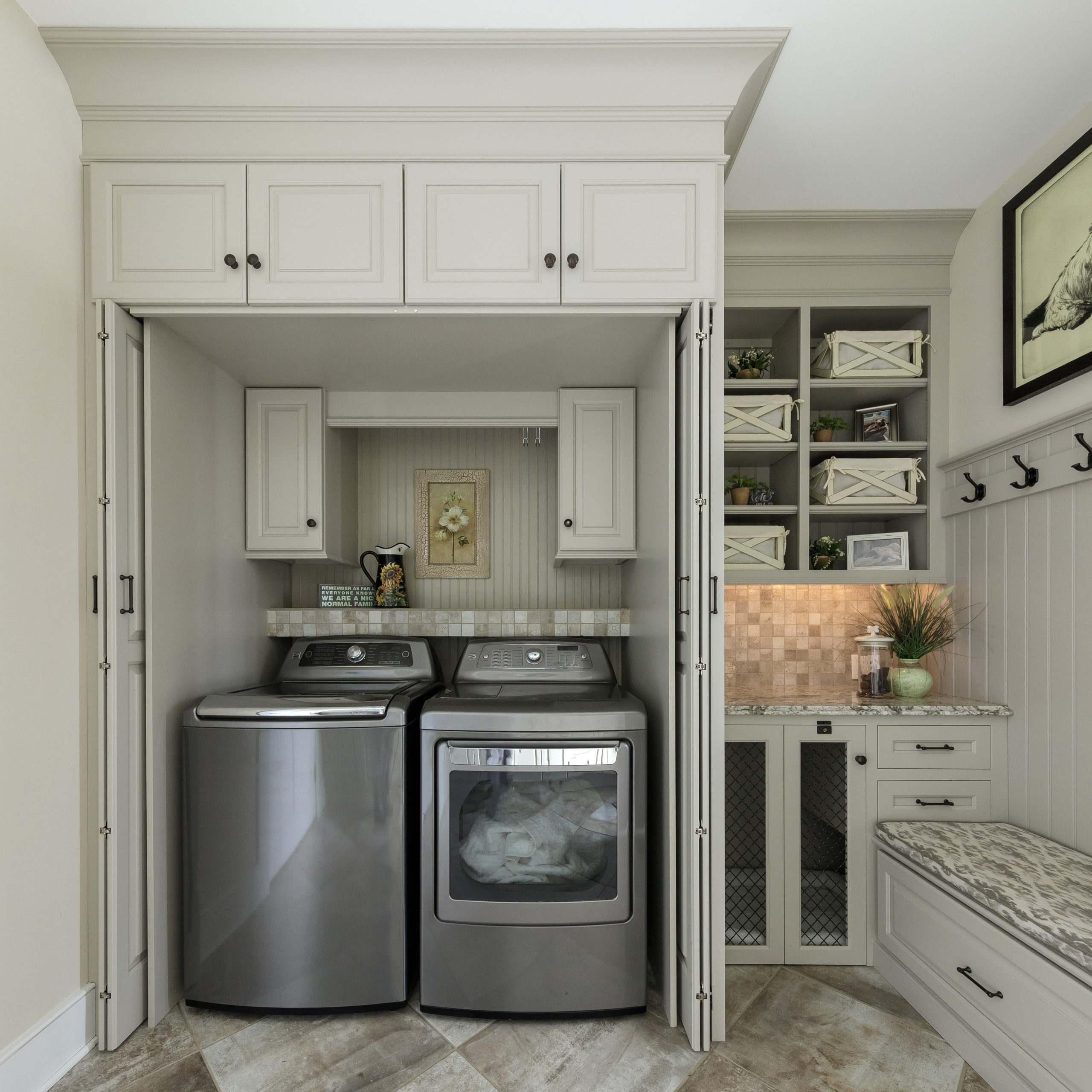 An impeccably organized laundry room showcasing custom cabinetry surrounding a washer and dryer setup, with convenient open shelving and a built-in sink.