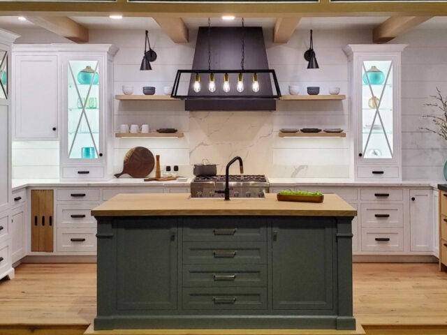 Modern kitchen with white upper cabinets and grey island base cabinets, featuring marble backsplash and wooden flooring.