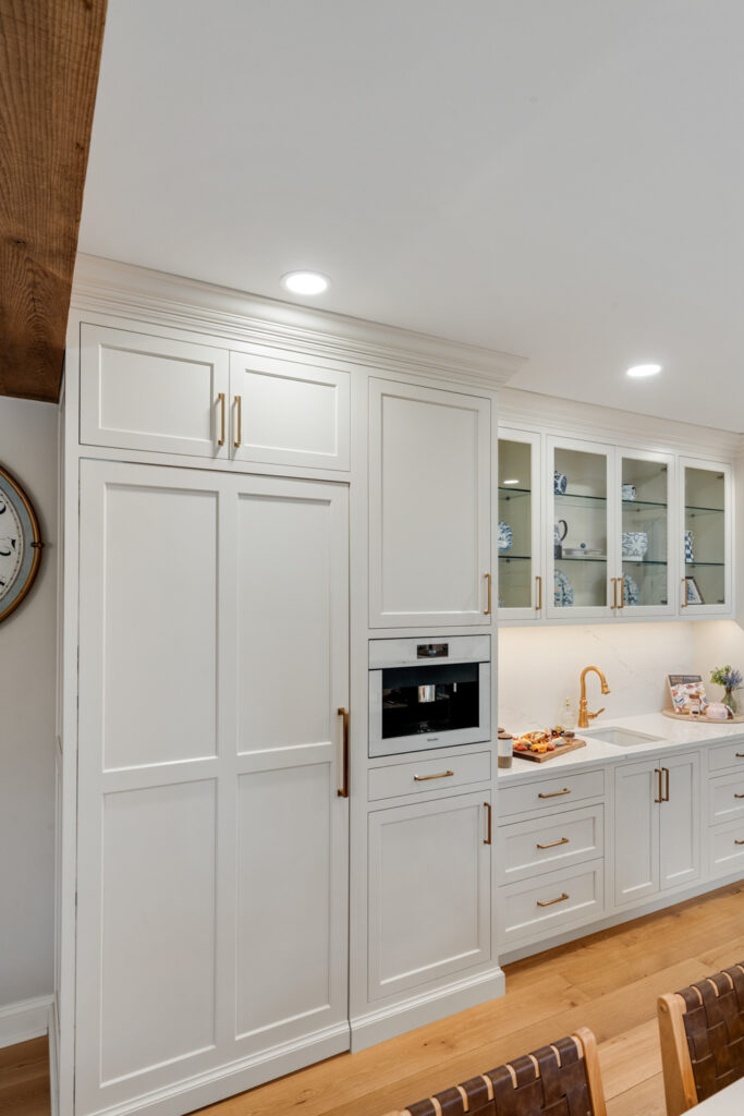 Custom white luxury cabinetry with gold hardware concealing a bespoke butler's pantry, illustrating seamless design and functionality.